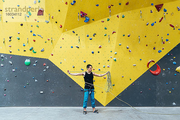 Mann  der ein langes Seil hält  steht vor der Kletterwand in der Halle.