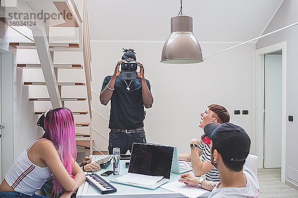 Eine Gruppe junger Männer und Frauen versammelte sich um einen Tisch und benutzte Laptops  Tablets und Virtual-Reality-Headsets.