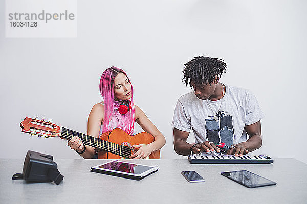 Junge Frau mit langen rosa Haaren und junger Mann mit kurzen Dreadlocks  die Gitarre und Keyboard spielen.