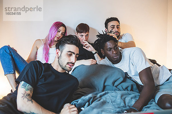 Gruppe junger Männer und Frauen  die auf einem Bett liegen und auf einen Laptop schauen.