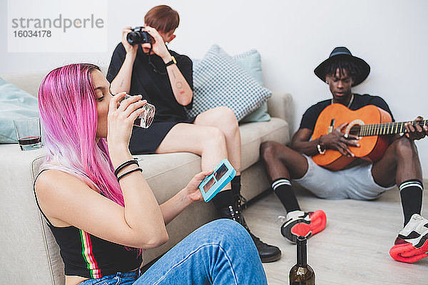 Gruppe junger Freunde in einer Wohnung  die Musik spielt  Wein trinkt und Fotos macht.
