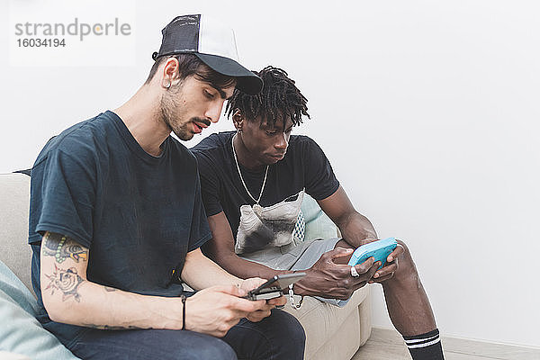 Zwei junge Männer sitzen auf einem Sofa und überprüfen ihre Mobiltelefone.