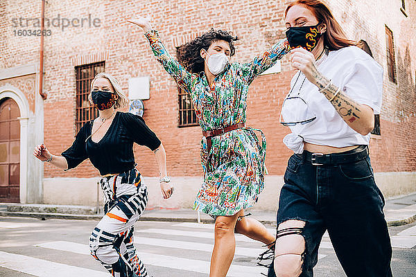 Drei junge Frauen mit Gesichtsmasken während des Corona-Virus  die in einer Straße über einen Fußgängerüberweg rannten.