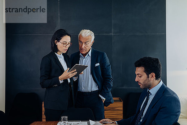 Geschäftsmann und -frau schauen auf digitales Tablet im Sitzungssaal