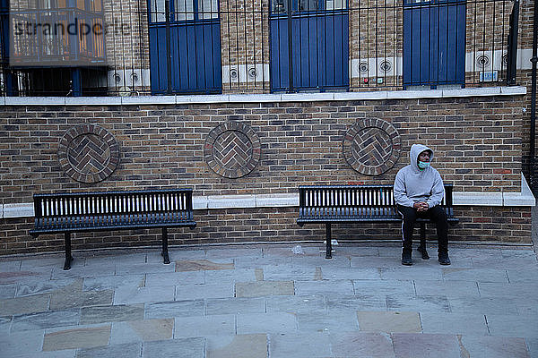 Mann mit Gesichtsmaske saß während der Corona-Virus-Krise auf einer Bank in Shoreditch  London.