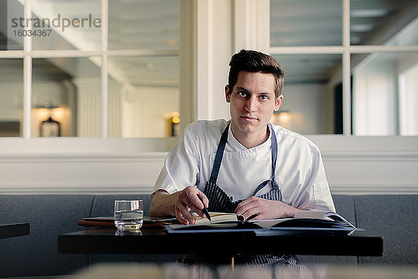 Junger männlicher Koch erledigt Papierkram und unterhält sich im Restaurant per Smartphone
