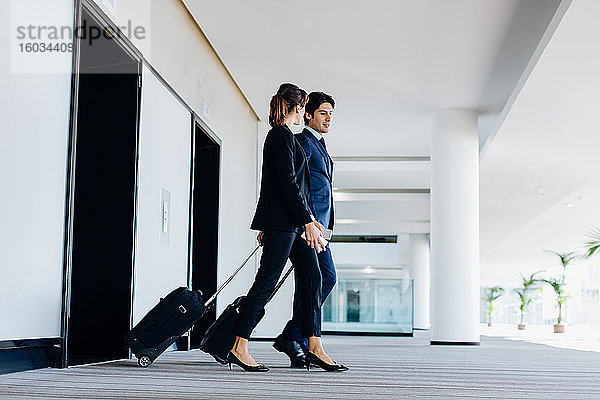 Geschäftsmann und Geschäftsfrau mit Rollgepäck beim Verlassen von Hotelrolltreppen