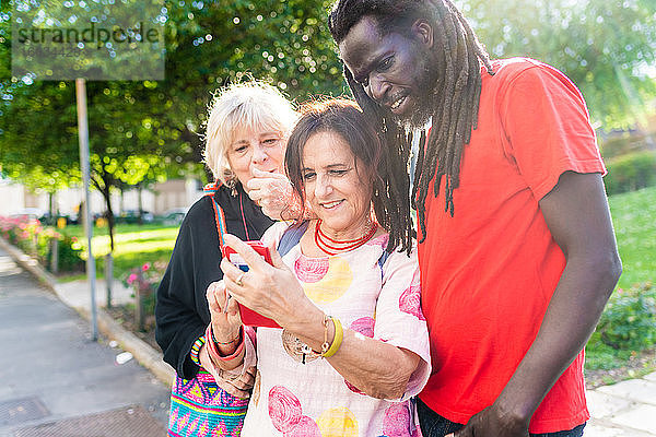Schwarzer Mann mit Dreadlocks und zwei kaukasische Frauen stehen auf der Brücke und schauen auf ein Mobiltelefon.