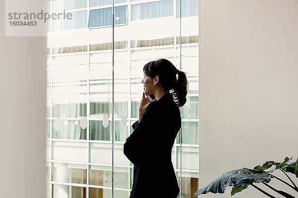 Geschäftsfrau mit Mobiltelefon am Fenster