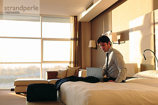 Geschäftsmann mit Laptop auf dem Bett eines Hotelzimmers