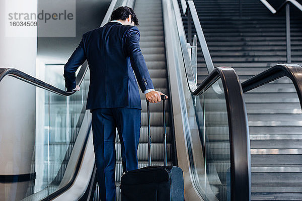 Geschäftsmann mit Rollgepäck auf der Hotelrolltreppe