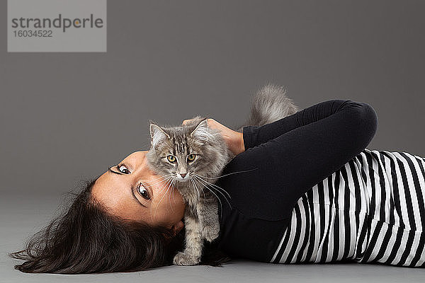 Studioaufnahme einer Frau  die eine graue Katze umarmt  auf grauem Hintergrund.