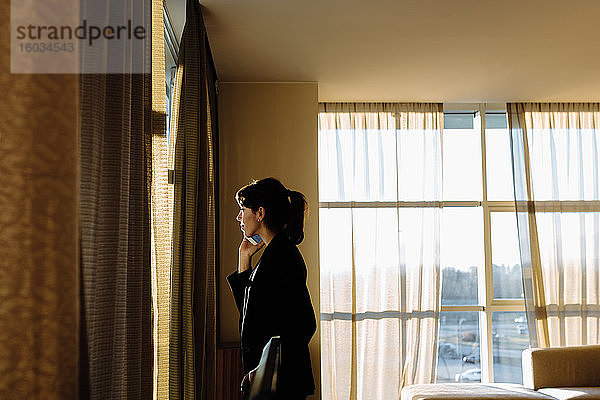 Geschäftsfrau mit Mobiltelefon am Fenster