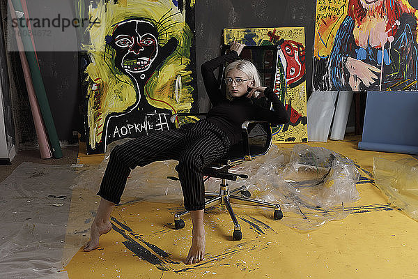 Porträt selbstbewusste  kühle junge Künstlerin im Atelier mit Gemälden