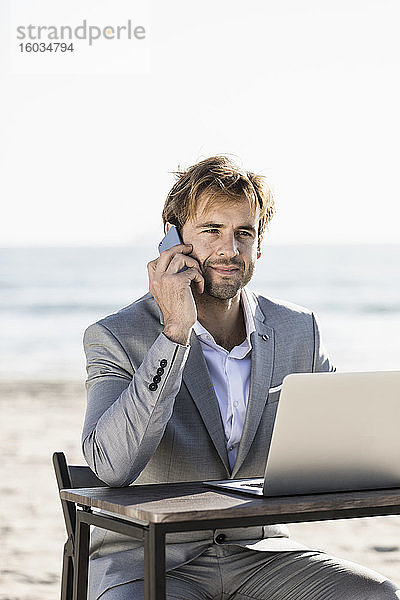 Geschäftsmann mit Smartphone und Laptop arbeitet am sonnigen Strand