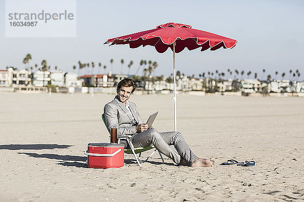 Porträt eines glücklichen barfüssigen Geschäftsmannes  der am sonnigen Strand arbeitet  Los Angeles  Kalifornien