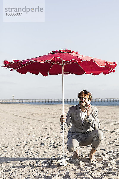 Geschäftsmann spricht mit einem Smartphone unter einem Sonnenschirm am sonnigen Strand  Los Angeles  Kalifornien