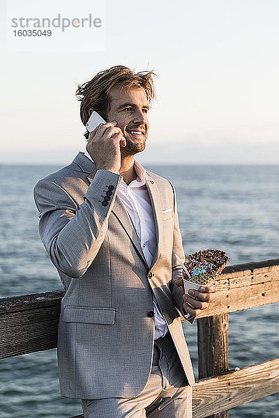 Geschäftsmann mit Eistüte spricht am Smartphone am Ozeanpier