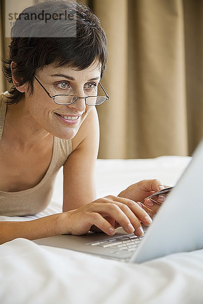 Frau Online-Shopping mit Kreditkarte und Laptop im Bett