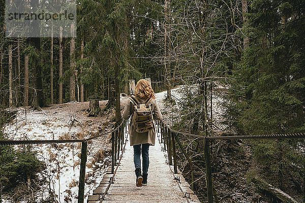 Rothaarige Frau mit Rucksack auf Steg in verschneiten Wäldern
