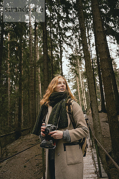 Rothaarige Frau mit Kamera auf Waldsteg