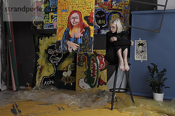 Barfüßige junge Künstlerin im Atelier mit Gemälden