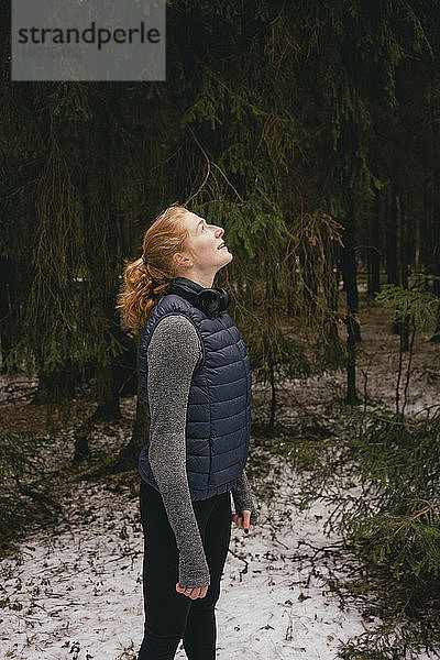 Gelassene rothaarige Frau schaut in verschneiten Wäldern auf