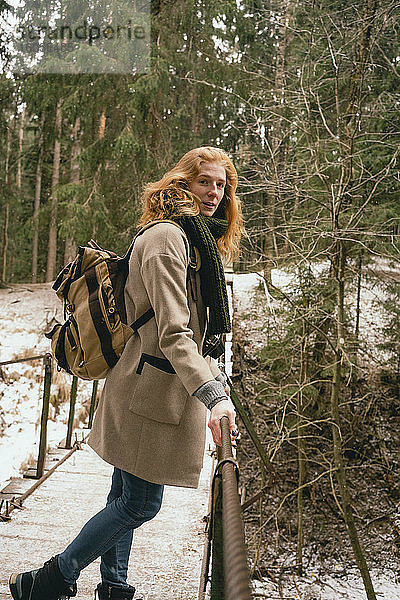 Porträt einer rothaarigen Frau mit Rucksack auf einem Steg in verschneiten Wäldern