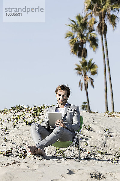Barfüßiger Geschäftsmann mit digitalem Tablet am sonnigen Strand  Los Angeles  Kalifornien