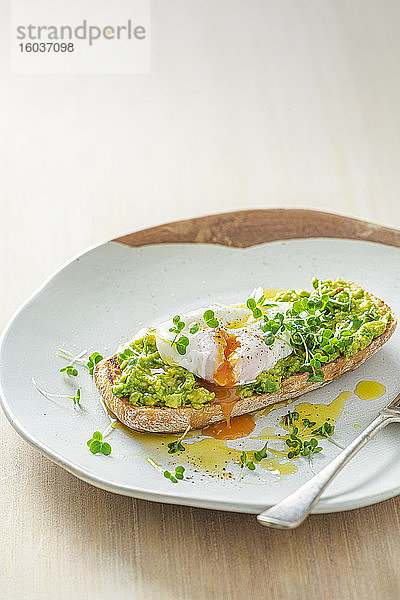 Pochiertes Ei auf Ciabatta-Toast mit zerdrückter Avocado  Kresse und Olivenöl