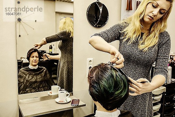 Friseurin schneidet einer Kundin die Haare vor einem Spiegel im Friseursalon  Köln  Nordrhein-Westfalen  Deutschland  Europa