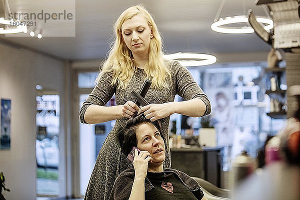 Friseurin frisiert einer telefonierenden Kundin die Haare im Friseursalon  Köln  Nordrhein-Westfalen  Deutschland  Europa