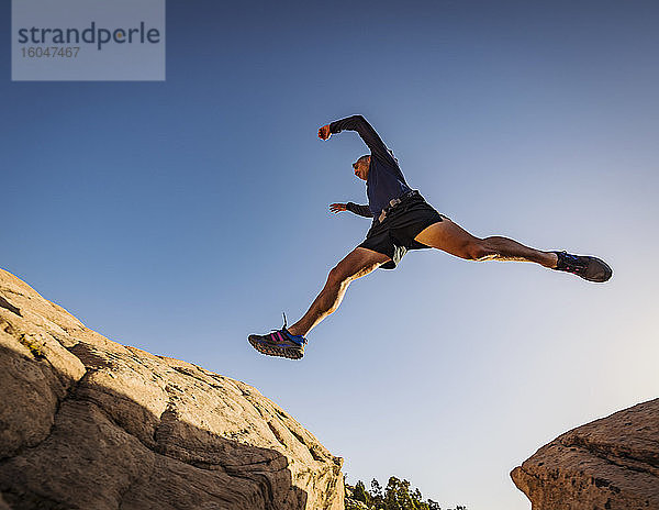 USA  Utah  St. George  Mann springt über Felsen  während er in erodierter Landschaft läuft