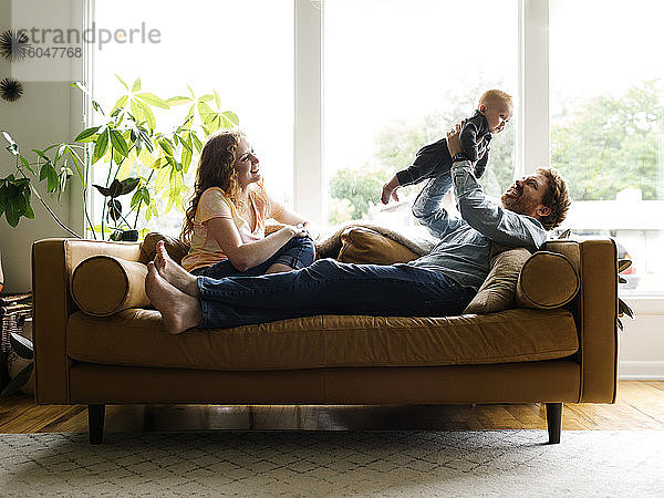 Mutter und Vater spielen mit dem kleinen Sohn (6-11 Monate) auf dem Sofa