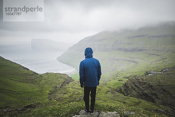 Dänemark  Mann steht auf einer Klippe über dem Meer und schaut auf die Aussicht