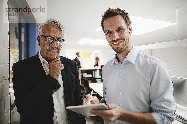 Zwei erfolgreiche Geschäftsleute stehen im Büro und benutzen ein digitales Tablet