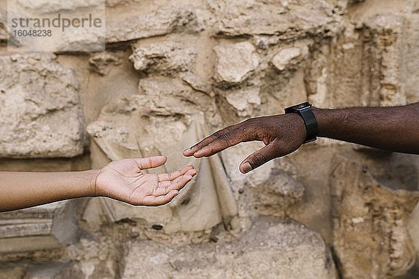 Abgeschnittene Hände eines Paares  das sich gegen eine Steinmauer streckt
