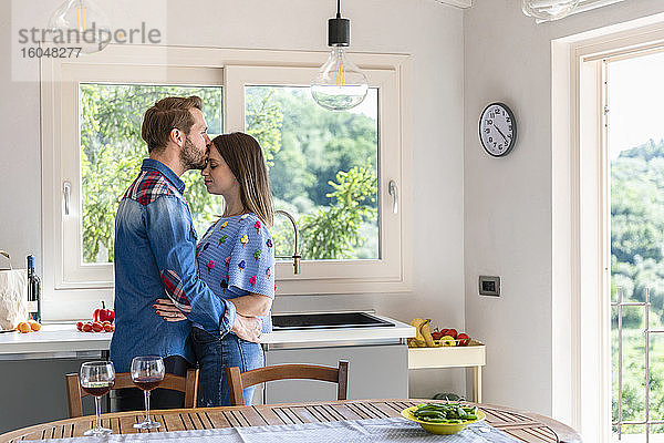 Mann küsst Frau  während er in der Küche zu Hause am Esstisch steht