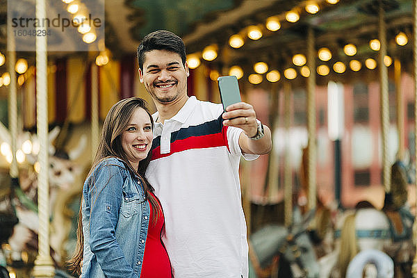 Glückliches schwangeres Paar  das ein Selfie mit seinem Smartphone im Vergnügungspark macht  Cascais  Portugal