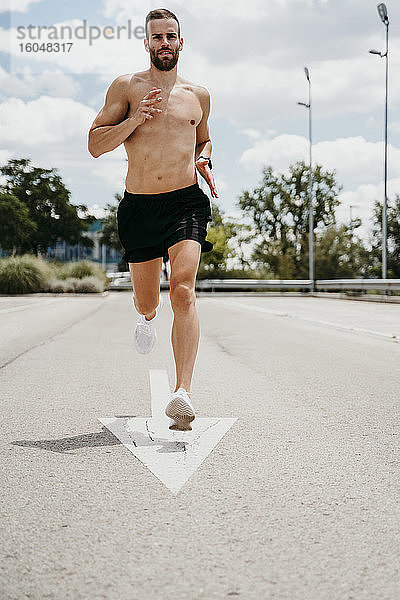 Männlicher Athlet mit nacktem Oberkörper  der mit einem Pfeilschild auf der Straße läuft