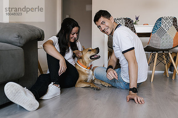 Lächelndes Paar sitzt mit Hund zu Hause auf dem Boden