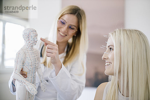Akupunktur  junge Frau mit Akupunkturnadel bei Behandlung im Gesicht  Arzt zeigt Akupunkturpunkt am Modell
