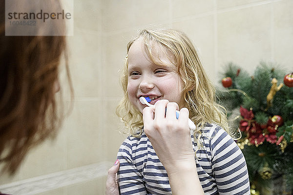 Ausgeschnittenes Bild einer Frau  die ihrer Tochter beim Zähneputzen zu Hause hilft