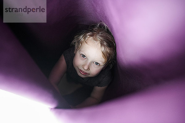 Nettes Mädchen versteckt sich im Vorhang zu Hause