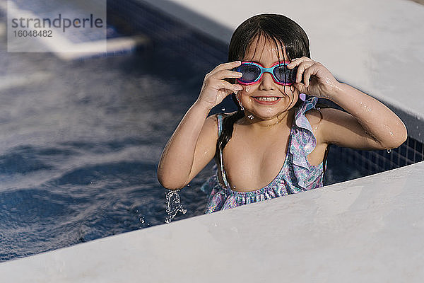 Porträt eines grinsenden kleinen Mädchens mit Schwimmbrille im Schwimmbecken