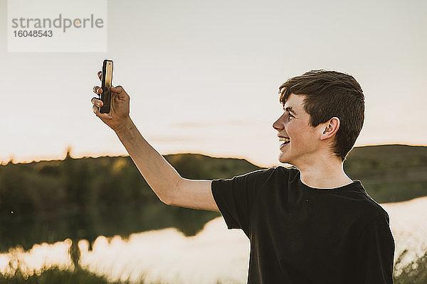 Glücklicher Teenager  der ein Selfie mit seinem Smartphone macht  während er bei Sonnenuntergang im Sumpf steht