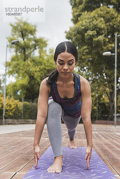 Junge flexible Frau übt Yoga auf einer Matte im Park