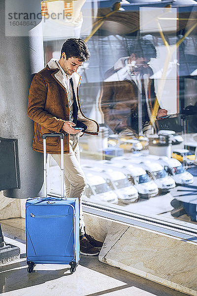 Geschäftsmann mit Smartphone am Fenster im Abflugbereich eines Flughafens