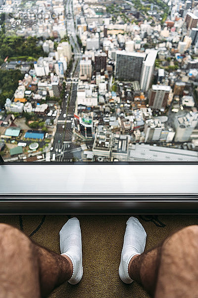 Japan  Präfektur Osaka  Osaka  Beine eines Mannes  der vor einem Fenster sitzt und auf die Stadt hinunterblickt