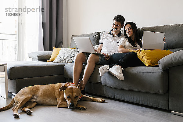 Ehepaar benutzt Laptops auf dem Sofa in der Nähe des Hundes zu Hause